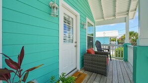 A turquoise house with a porch, a wicker chair, and a welcome mat.
