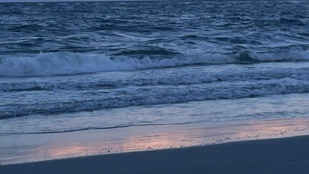 A beach with waves and a sunset sky.