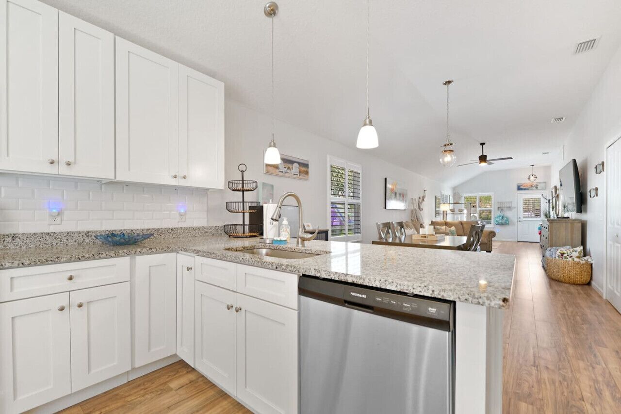 A modern kitchen with white cabinetry, granite countertops, and a dishwasher.