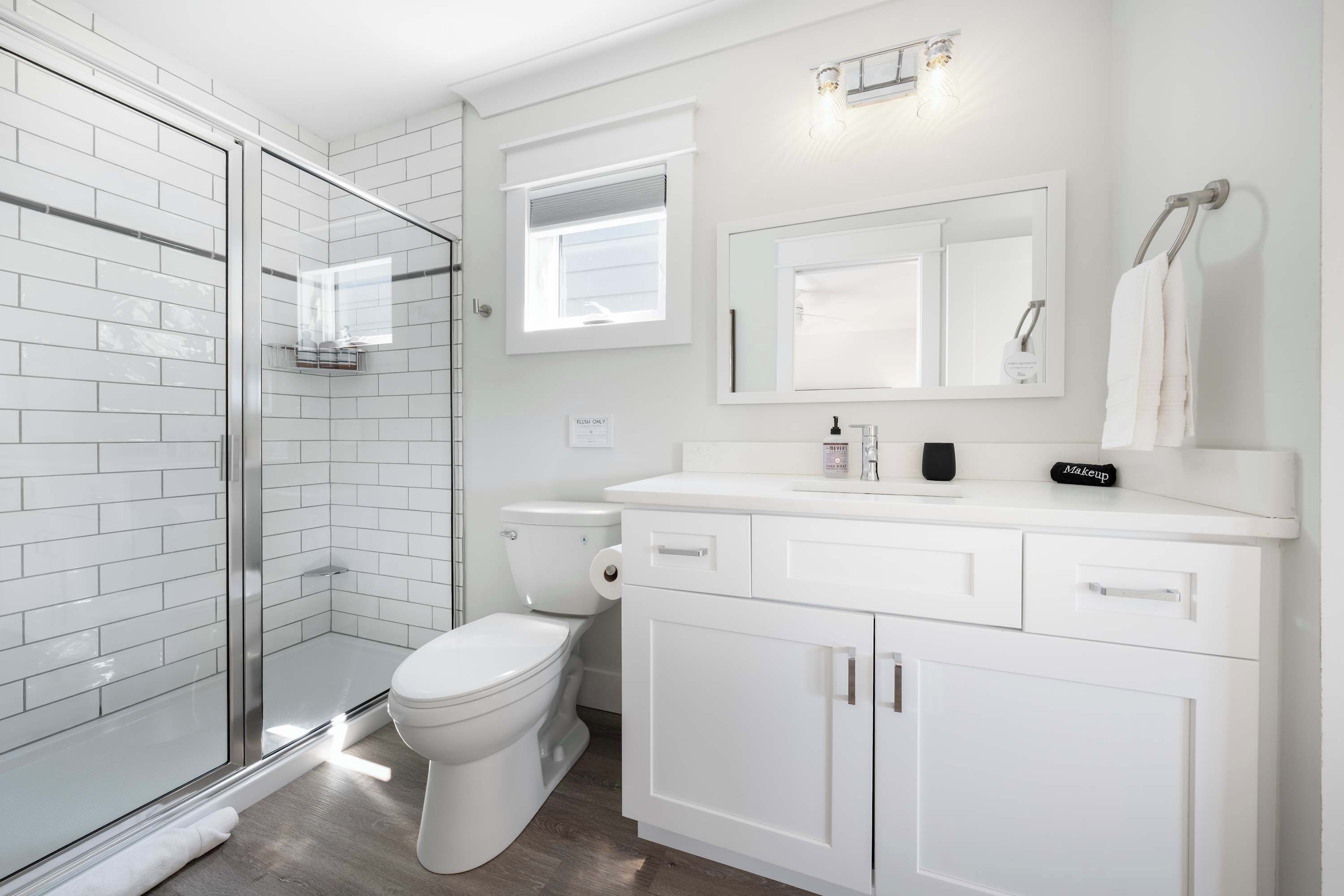 Ein modernes Badezimmer mit Duschkabine aus Glas, Toilette, Waschbecken mit Spiegel und Handtuchhalter.