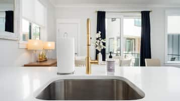 A modern kitchen with a stainless steel sink, a white countertop, and a gold faucet.