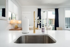 A modern kitchen with a stainless steel sink, a white countertop, and a gold faucet.