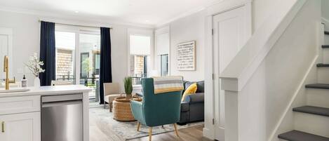 A modern kitchen with a dishwasher, a dining area with a table and chairs, a sofa, and a staircase.