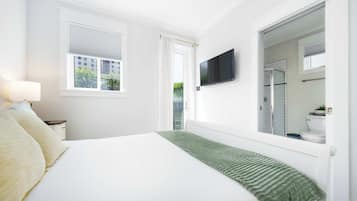 Ein Schlafzimmer mit einem Bett, einem an der Wand montierten Fernseher und einem Fenster mit Jalousien.