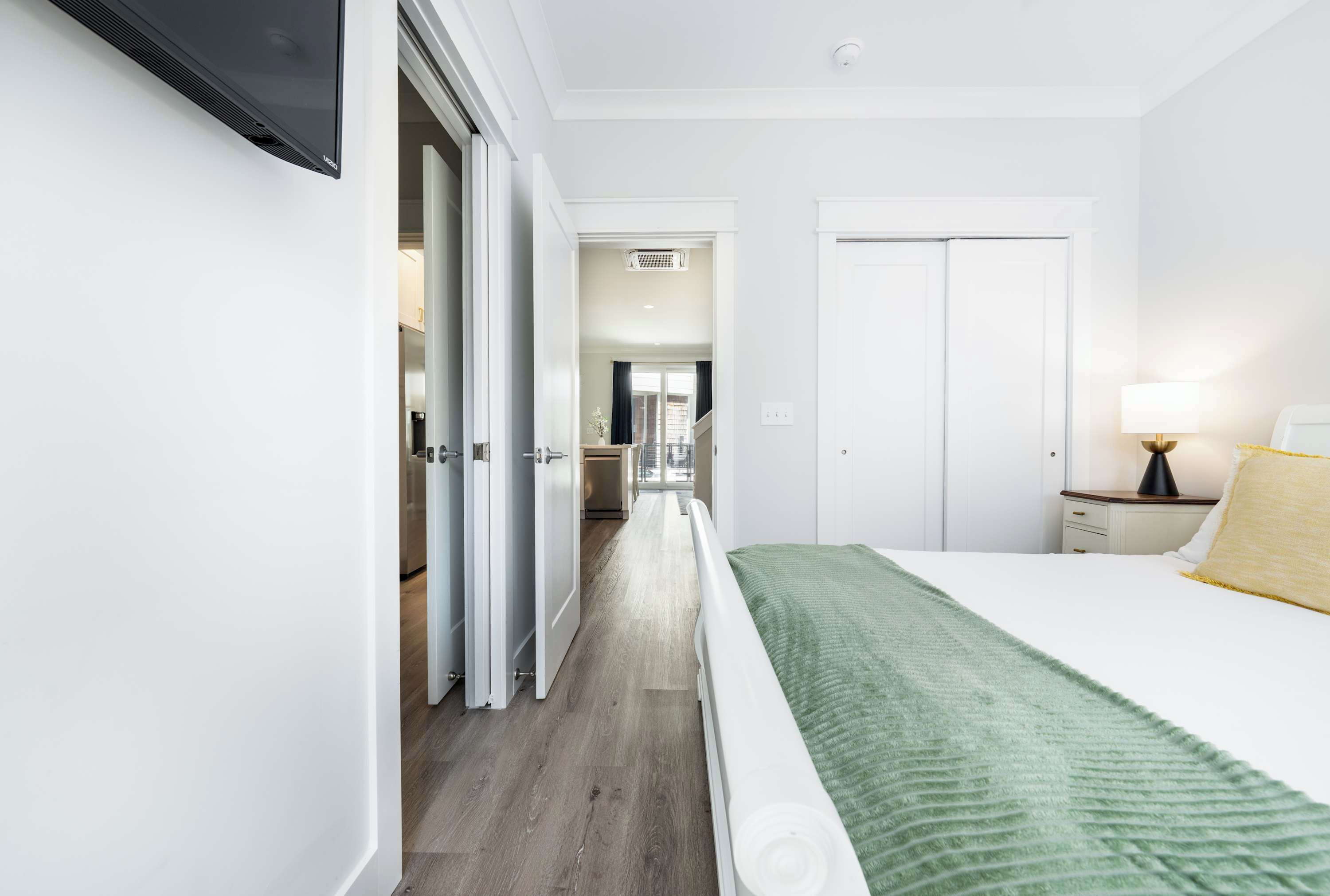 Et hotelværelse med en seng, et natbord, en lampe og udsigt til gangen.