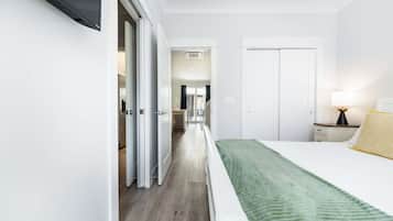 Et hotelværelse med en seng, et natbord, en lampe og udsigt til gangen.