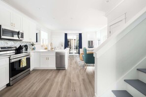 A modern kitchen with white cabinetry, stainless appliances, and a wooden floor.