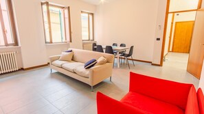 A modern living room with a beige sofa, a red armchair, and a dining area with a table and chairs. - Piazza Garibaldi - Italian Homing (Desenzano del Garda)