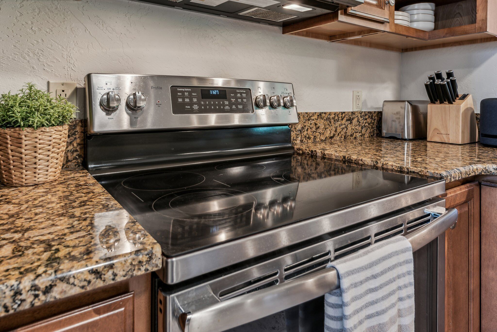 A stainless steel oven with a digital control panel, a granite countertop, and wooden cabinets.