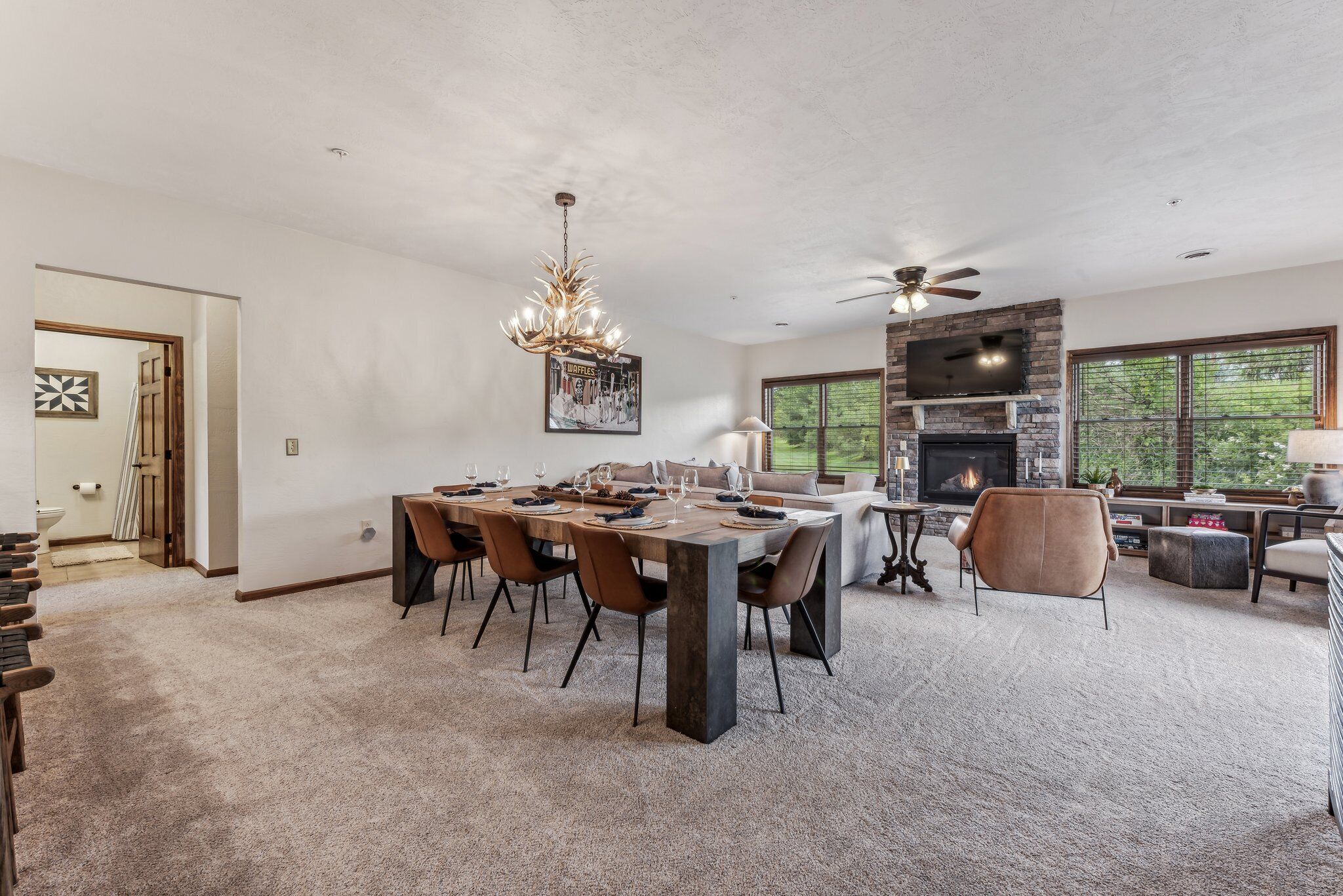 A spacious living room with a fireplace, a dining area with a large table and chairs, and a ceiling fan.