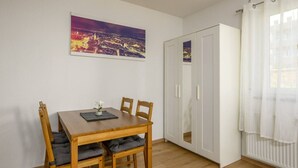 A room with a wooden dining table, four chairs, a white wardrobe, and a cityscape painting on the wall. - Arbio I Spacious Apart near Auensee (Leipzig)
