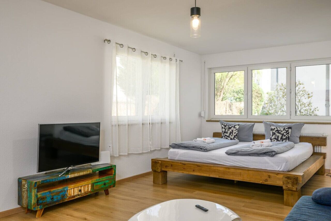 A bedroom with a wooden bed, a TV on a wooden cabinet, and a window with curtains.