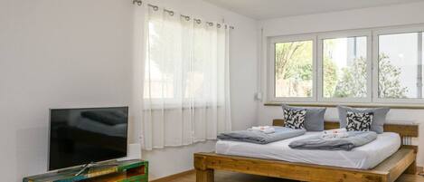 A bedroom with a wooden bed, a TV on a wooden cabinet, and a window with curtains.