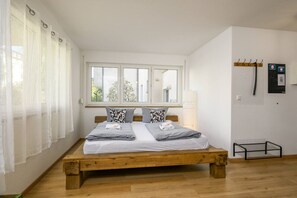 Un dormitorio con una cama de madera, cortinas blancas, una ventana y un perchero en la pared.