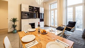 Una sala de estar moderna con una mesa de comedor preparada para cuatro personas, un sofá, una silla y un ventanal con cortinas.