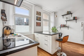 A modern kitchen with a large window, white cabinetry, a black countertop, and a bar stool. - Arbio I Retro Apart in Leipzig center (Leipzig)