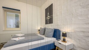 A bedroom with a bed, a nightstand, a lamp, a window, and a wall-mounted picture. - Arbio I Industrial Studio in Leipzig Bayerischer (Leipzig)