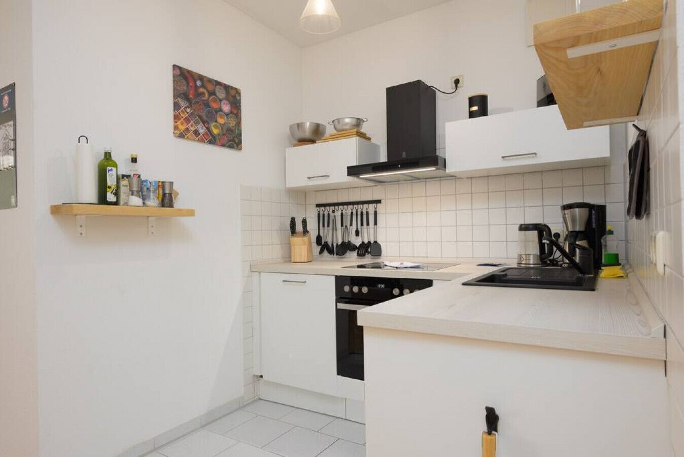 A modern kitchen with white cabinets, a stove, a coffee maker, and a hanging pot rack.