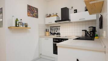 A modern kitchen with white cabinets, a stove, a coffee maker, and a hanging pot rack.