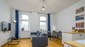 Un salon moderne avec un canapé gris, un plancher en bois, un téléviseur et un coin repas comprenant des chaises et une table.