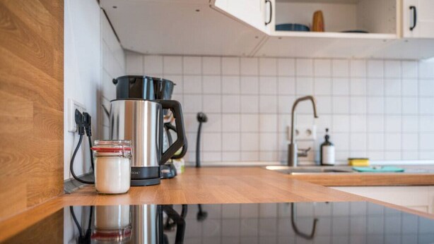A kitchen with a stainless steel coffee maker, a glass jar with a red lid, and a black electric kettle on a wooden countertop. - Arbio I Retro Apart near Grassi Museum (Leipzig)