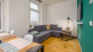 A modern living room with a grey sectional sofa, a wooden dining table, and a small side table with a lamp.