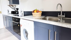 Une cuisine moderne équipée d’un lave-linge encastré, d’un évier et d’un panier à fruits posé sur le plan de travail.