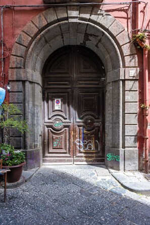 Un arco in pietra che conduce a una porta di legno scura, con graffiti e un cartello 'No Parking'.