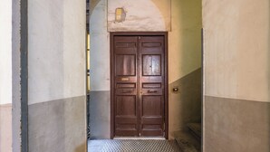 Un couloir avec une double porte en bois, un sol à carreaux et une petite marche menant à la porte.