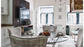 A modern kitchen with a dining area, featuring a round glass table, white chairs, and a built-in oven. - Blissful Bradford Apartment - City Center Gem (Bradford)