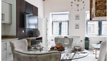 A modern kitchen with a dining area, featuring a round glass table, white chairs, and a built-in oven.
