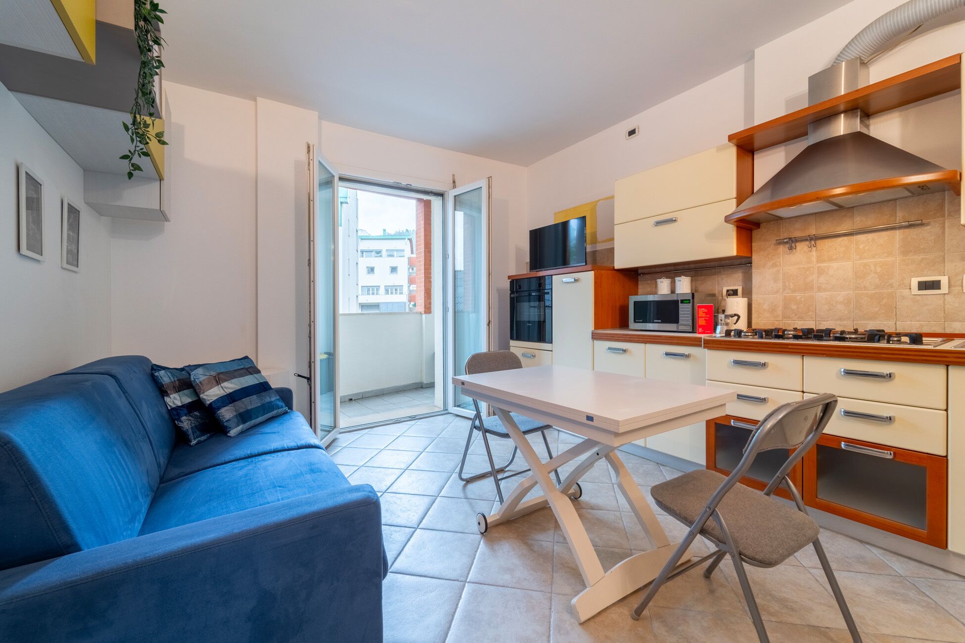 Un espace de vie compact comprenant un canapé, une table pliante et un coin cuisine équipé d’un four à micro-ondes et d’une cuisinière.