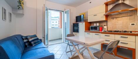 A compact living space with a sofa, a foldable table, and a kitchen area including a microwave and stove.