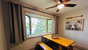 Ein Zimmer mit Holztisch und Bänken, einem Deckenventilator, einem Fenster mit Vorhängen und einem Bärenbild an der Wand.