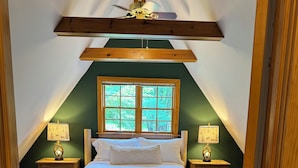 A bedroom with a sloped ceiling, a wooden bed frame, two bedside tables with lamps, and a window with a view of greenery. - Luxury Poconos Chalet - Hot Tub, Fire Pit, Wineries , Breweries & Pet-Friendly!! (Albrightsville)