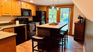 A kitchen with wooden cabinets, a black stove, a microwave, and a refrigerator. There is a wooden island with a sink and two stools. - Luxury Poconos Chalet - Hot Tub, Fire Pit, Wineries , Breweries & Pet-Friendly!! (Albrightsville)