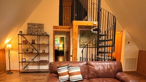 A spacious loft with a brown leather sofa, a wooden staircase, and a metal railing. - Luxury Poconos Chalet - Hot Tub, Fire Pit, Wineries , Breweries & Pet-Friendly!! (Albrightsville)
