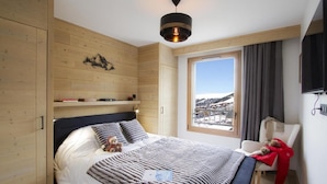 Une chambre à coucher comprenant un lit, une chaise, un téléviseur, une fenêtre avec vue et un lambris en bois.