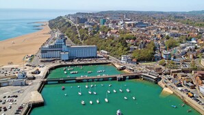A coastal town with a marina filled with boats, a large hotel with multiple floors, and a beach area. - Minutes from Folkestone Central Station and modern flat with three bedrooms. (Cheriton, near Folkestone)
