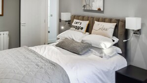 A neatly made bed with a quilted grey duvet, two pillows with text, and a bedside table with a lamp. - Minutes from Folkestone Central Station and modern flat with three bedrooms. (Cheriton, near Folkestone)