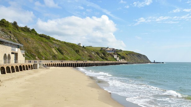A beach with a stone pier extending into the sea, a grassy hill with buildings, and a clear sky. - Minutes from Folkestone Central Station and modern flat with three bedrooms. (Cheriton, near Folkestone)