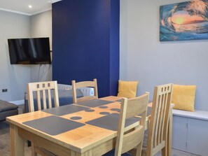 Un coin repas avec une table et des chaises en bois, un téléviseur à écran plat fixé au mur et un tableau au-dessus de la table.