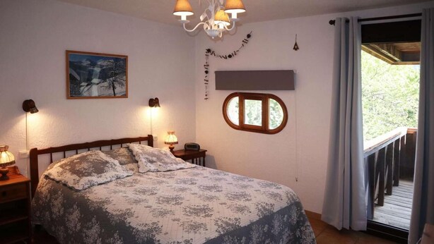 Ein Schlafzimmer mit Bett, Nachttisch, Lampe, einem Gemälde, einem Fenster und einem Balkon.