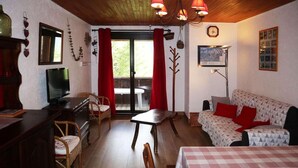 Ein gemütliches Wohnzimmer mit einer Couch, einem Esstisch, einem Fernseher und einer Holzbalkendecke.