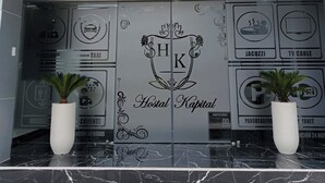 L’entrée d’un hôtel au design moderne, avec un logo comprenant les lettres « HK » et le nom « Hotel Capital » apposé sur la porte en verre, des plantes en pot de chaque côté et un sol en marbre.