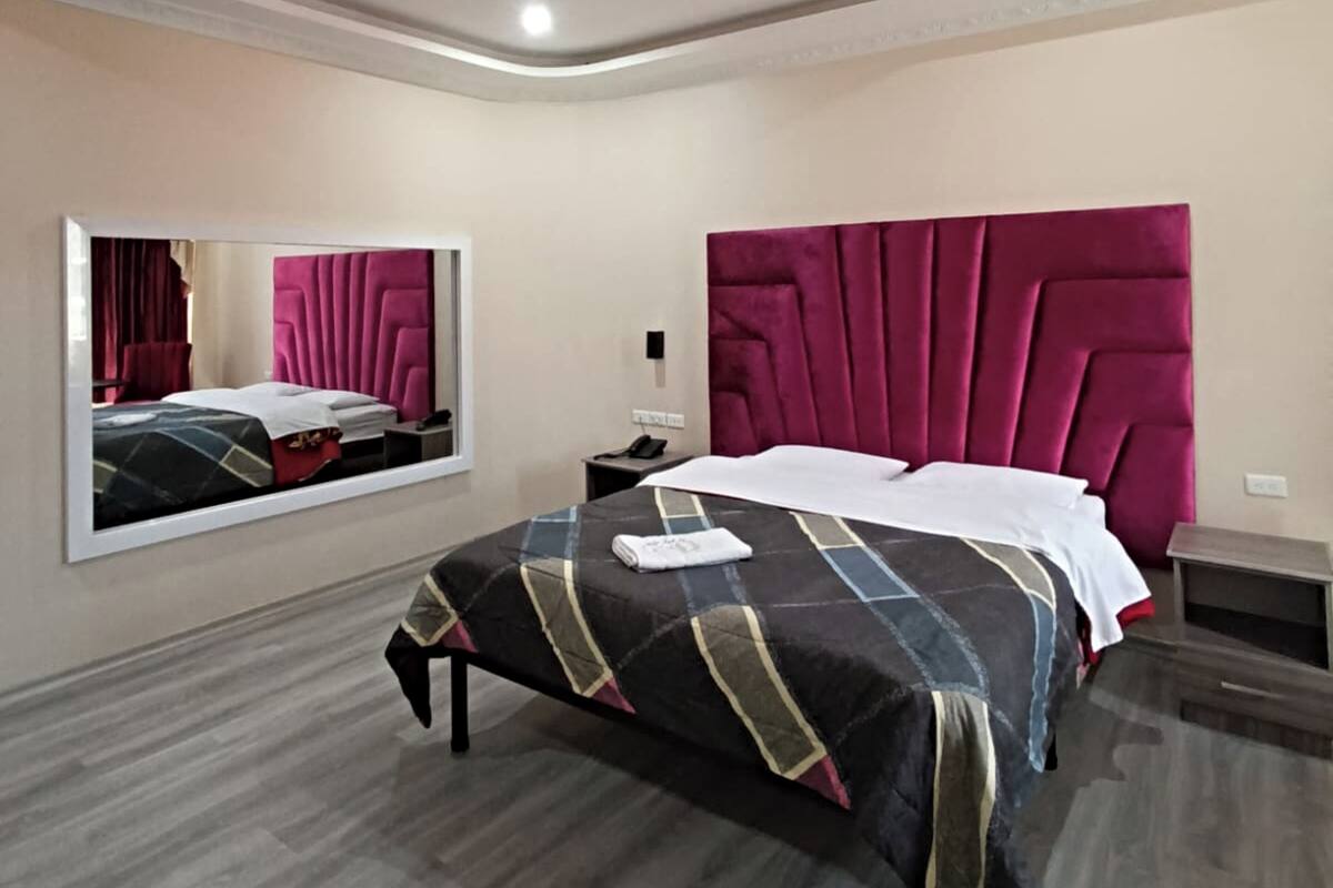A modern bedroom with a large bed, a mirror, and a unique ceiling design.