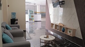 Un hall d’entrée moderne avec un canapé, une petite table ronde, un distributeur d’eau et un téléviseur fixé au mur.