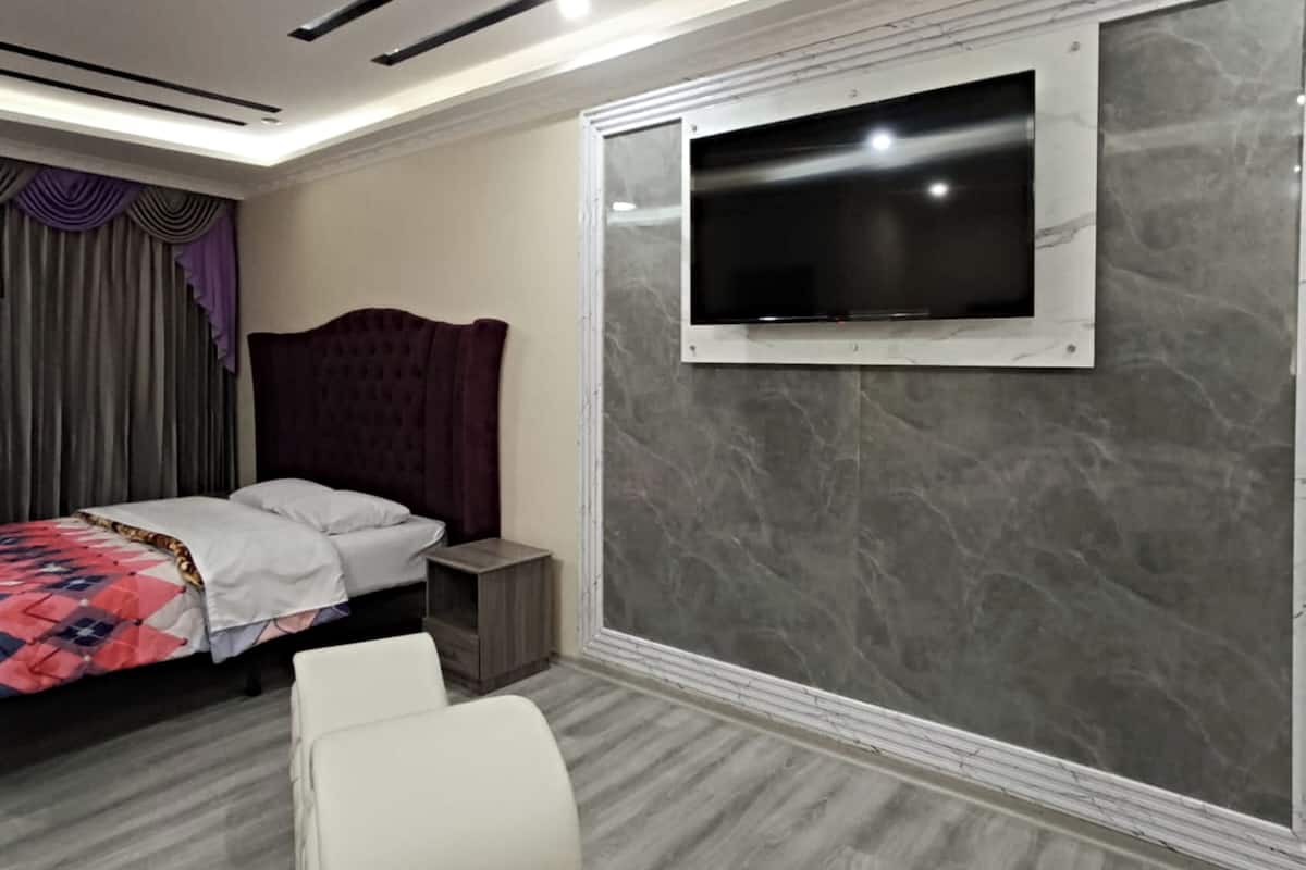 A modern bedroom with a bed, a TV mounted on the wall, and a small bedside table.