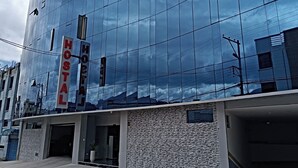 Un hôtel moderne avec une façade en verre réfléchissant, une enseigne « HOSTAL » bien visible et une entrée à l’aspect pierre.