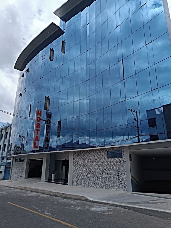 A modern hotel with a reflective glass facade, a prominent "HOSTAL" sign, and a stone-textured entrance.
